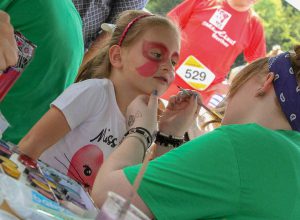 Familien.Spiele.Fest | Ein Mädchen wird geschminkt und lächelt erwartungsvoll. Inklusion in allen Bereichen.